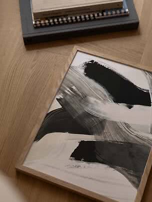 Framed abstract black-and-white print on a wooden floor beside a stack of books