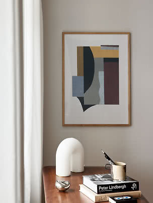 Framed abstract wall art above a wooden table with books, mug and white sculpture by curtain