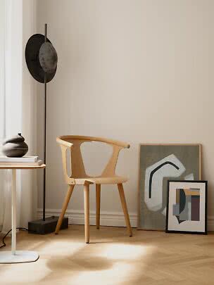 Light wood chair in a minimalist corner with black floor lamp and framed abstract art