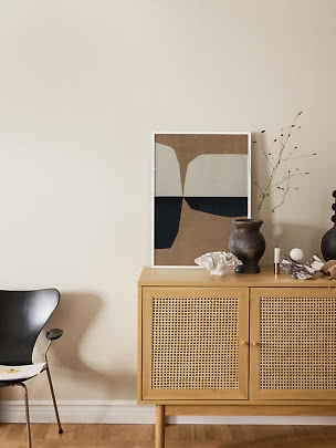 Light wood cabinet with cane doors, abstract print, dark vase and decor against a beige wall