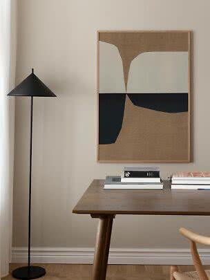Abstract framed wall art above a wooden table with books and a black floor lamp