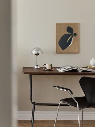 Schreibtisch mit Chromlampe, Tasse, offenem Buch und abstrakter Wandkunst im minimalistischen Raum