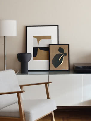 Modernes Wohnzimmer mit Sessel, Sideboard und zwei abstrakten Bildern in schwarzen Rahmen