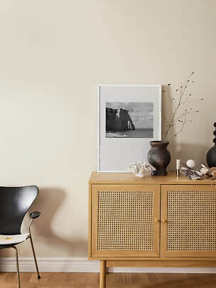 Light wood cabinet with cane doors, vase, coral and framed black-and-white photo against beige wall