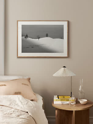 Gerahmtes Schwarz-Weiß-Foto von schneebedeckten Hügeln mit vereinzelten Bäumen über einem Bett