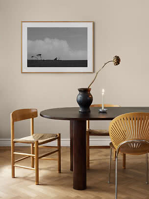 Essecke mit rundem dunklem Holztisch, Stühlen, schwarzer Vase, Kerze und gerahmtem Schwarzweißfoto
