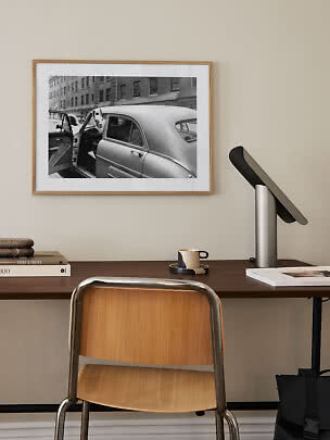 Schreibtisch mit Holzstuhl, schwarzer Tischlampe und gerahmtem Schwarz-Weiß-Foto an der Wand