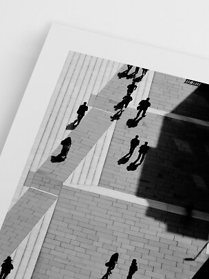 Black-and-white print showing people and long shadows from above on a tiled plaza