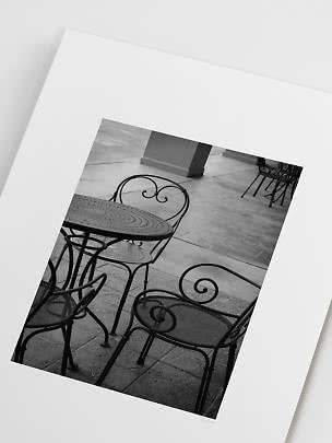 Impresión fotográfica en blanco y negro de mesa y sillas de hierro en patio de piedra