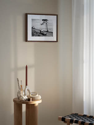 Ingelijste zwart-wit kustfoto aan beige muur boven houten tafeltje met kaars en accessoires