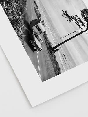 Zwart-witfoto van oldtimer met caravan op kustweg bij een scheve boom