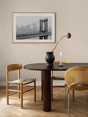 Dining area with round dark table, wooden chairs, vase with dried flower, candle and framed bridge photo