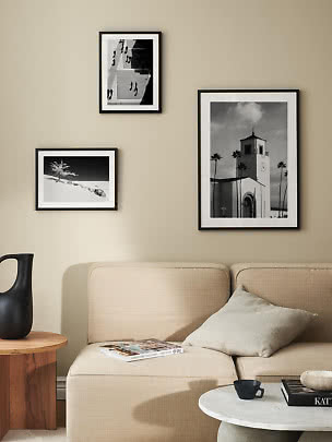 Três fotografias em preto e branco emolduradas sobre um sofá bege numa sala moderna.