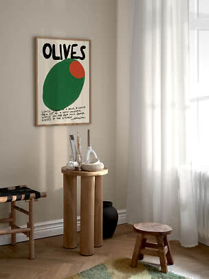 Indrammet OLIVES-plakat med stor grøn oliven på beige væg over et rundt træbord