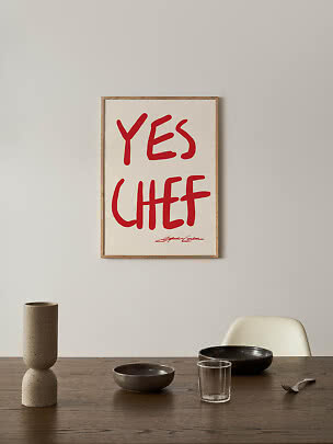 Indrammet plakat med rød håndskrift "YES CHEF" over et spisebord.