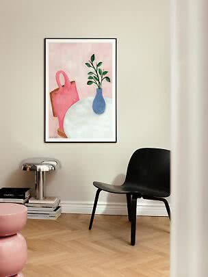 Indrammet kunsttryk med lyserød taske og blå vase med grønne grene på væg i moderne stue