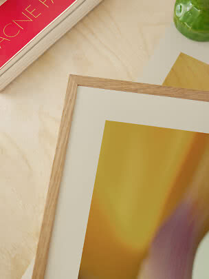 Gerahmter Kunstdruck auf hellem Holztisch neben rotem Buch und grüner Vase