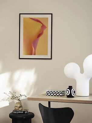 Affiche florale encadrée sur mur beige au-dessus d'une table avec vase noir et blanc et lampe blanche