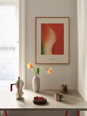 Angolo cucina luminoso con poster astratto, vaso con fiori arancioni, caffettiera, tazza e pomodori.