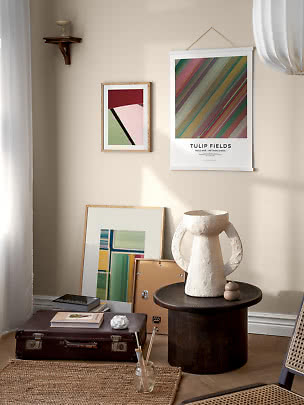Mysig hörna med färgglada posters, stor vit vas på mörkt sidobord och ramar mot väggen