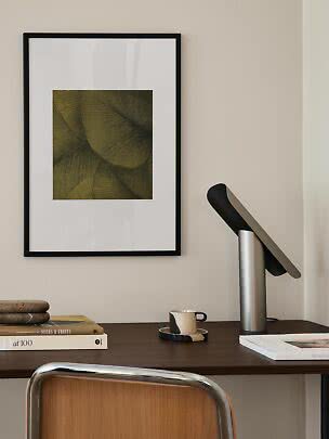 Schreibtisch mit schwarzer Tischlampe, Tasse und gerahmter abstrakter Kunst an der Wand
