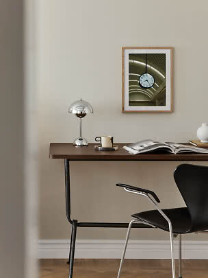 Minimalistisch bureau met chromen lamp, mok, open boek en ingelijste wandprint