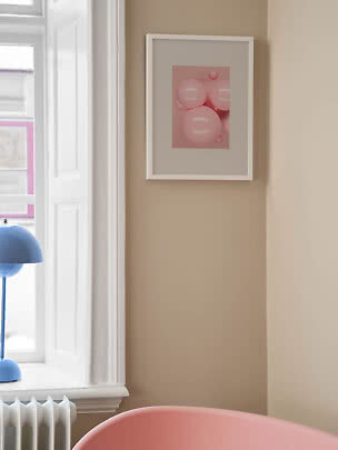Stampa artistica rosa con bolle in cornice bianca su parete beige accanto a una finestra
