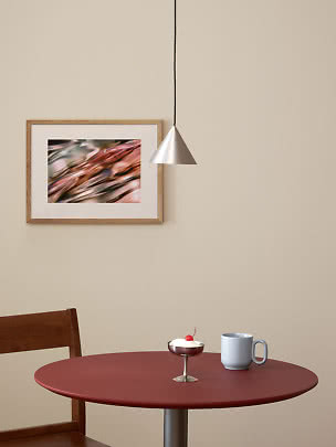 Tavolo rotondo rosso con tazza azzurra e piccolo dessert sotto lampada a sospensione argentata.