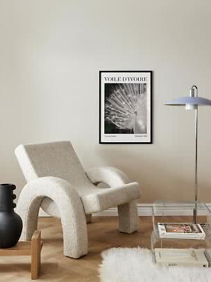 Affiche encadrée d’un paon blanc sur mur beige au-dessus d’un fauteuil bouclé crème