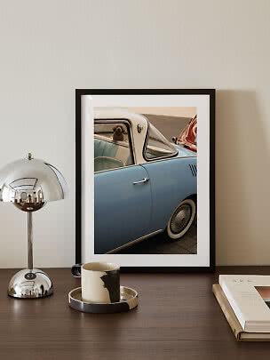 Foto enmarcada de coche vintage azul claro con un perro pequeño en la ventana sobre mesa oscura