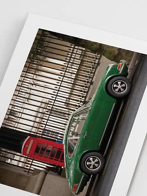 Green classic sports car parked by a red telephone box in front of a black iron fence
