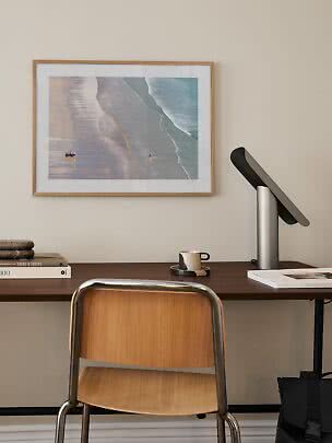 Home office with wooden desk, chair, table lamp and framed beach print on the wall