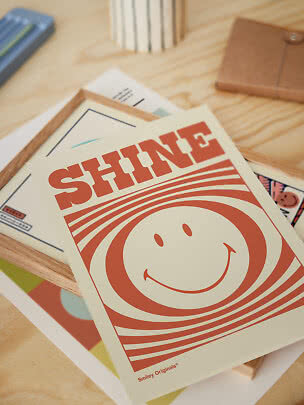 Poster met de tekst SHINE en een smiley op een bureau met lijsten en papier