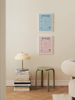 Due poster Space incorniciati, blu e rosa, sopra uno sgabello verde e una lampada su libri