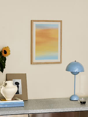 Abstraktes gerahmtes Poster über einem Sideboard mit blauer Lampe, Vase und Sonnenblume