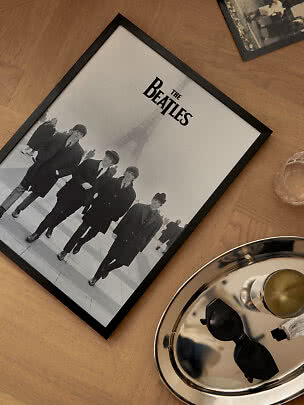 Indrammet sort-hvid Beatles-plakat på trægulv med bakke og solbriller ved siden af