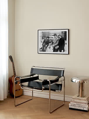 Black cantilever chair with steel frame beside guitar and silver lamp under a framed black-and-white photo