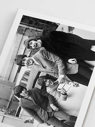Black-and-white photo of four young people smiling beside a car