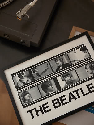 Platine vinyle à côté d’une affiche encadrée des Beatles sur table sombre