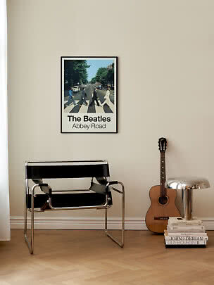 Poster incorniciato The Beatles Abbey Road su parete beige sopra una sedia nera tubolare.