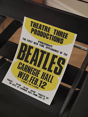 Poster giallo e bianco dei Beatles appoggiato a una sedia nera