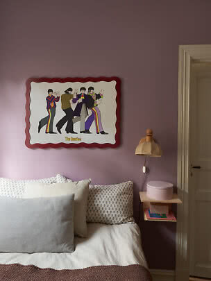 Soveværelse med lilla væg, seng, natbord og farverigt Beatles-billede over sengen