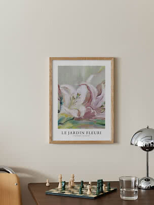 Ingelijste bloemenposter aan de muur boven een tafel met schaakbord, glas en chromen lamp