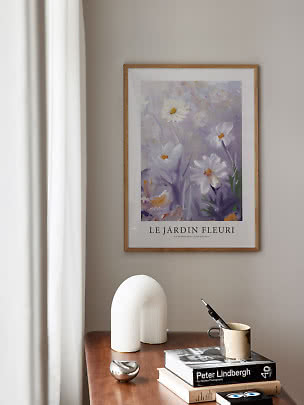Inramad blomsteraffisch över träbord med böcker, mugg och vit skulptural lampa