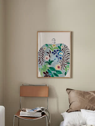 Framed colorful art print with woman and flowers above chair beside bed