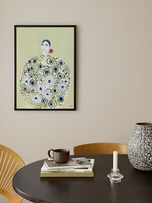 Affiche encadrée d’une femme en robe fleurie sur mur beige au-dessus d’une table
