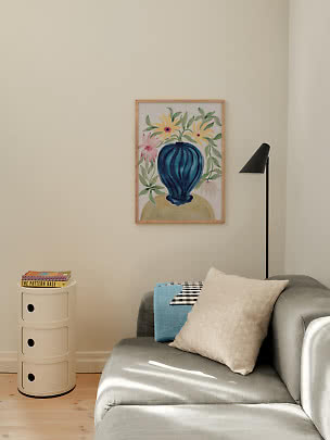 Living room corner with gray sofa, black floor lamp and framed floral print with blue vase on beige wall