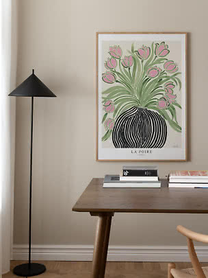 Indrammet plakat med lyserøde tulipaner i sort vase over et træbord ved siden af en sort gulvlampe