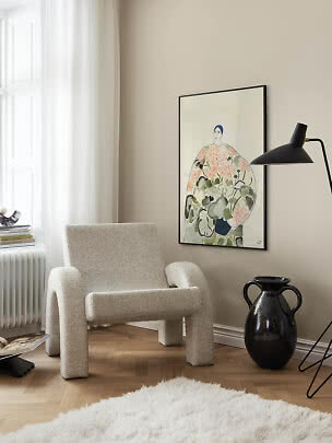 Lys stue med bouclé-lænestol, sort gulvlampe og indrammet kunstplakat på beige væg