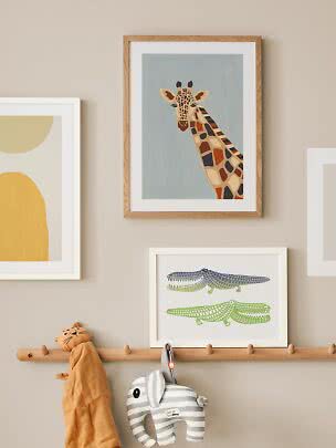Déco murale enfant avec affiche girafe encadrée au-dessus d’un porte-manteau et d’un éléphant doux